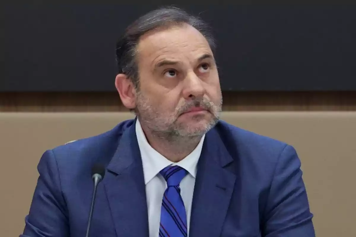 Hombre con traje azul y corbata a rayas mirando hacia arriba en una sala de conferencias.