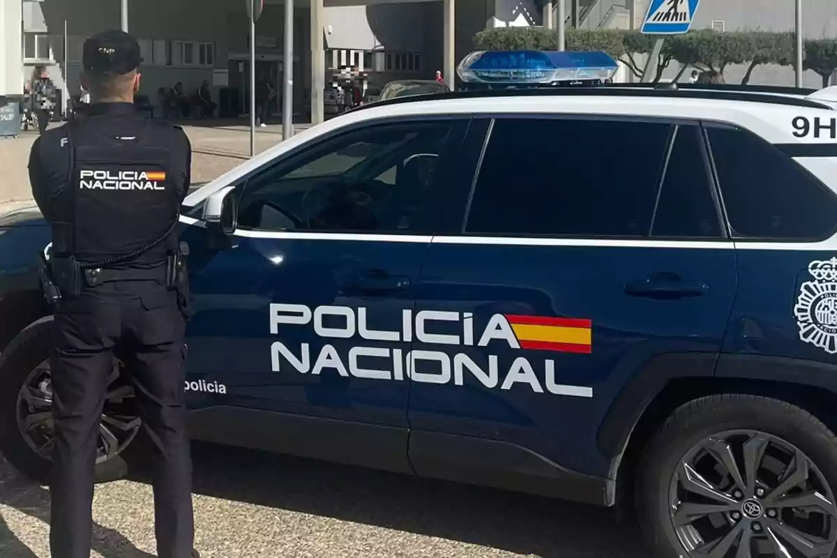 Un agente de la Policía Nacional de pie junto a un vehículo oficial en una zona urbana.