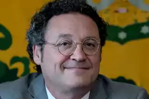 Man with glasses and curly hair smiling, with a yellow and green background.