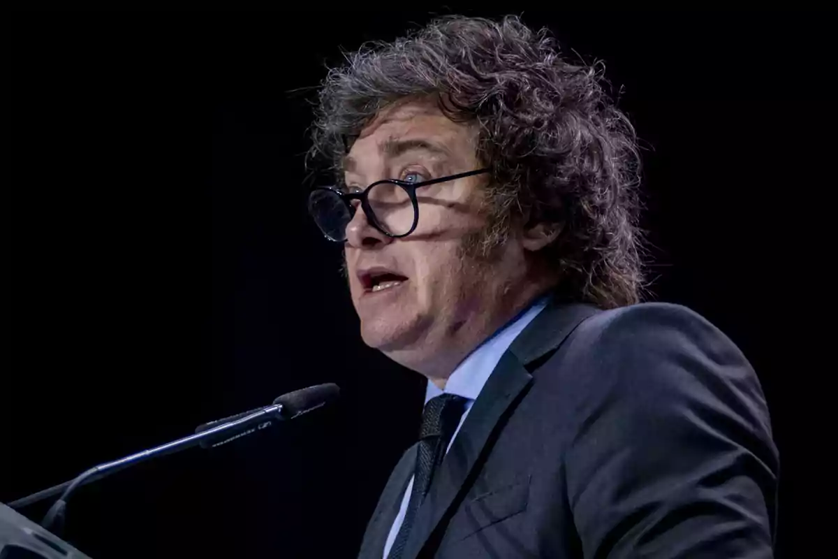 Hombre con gafas y cabello rizado hablando en un micrófono.