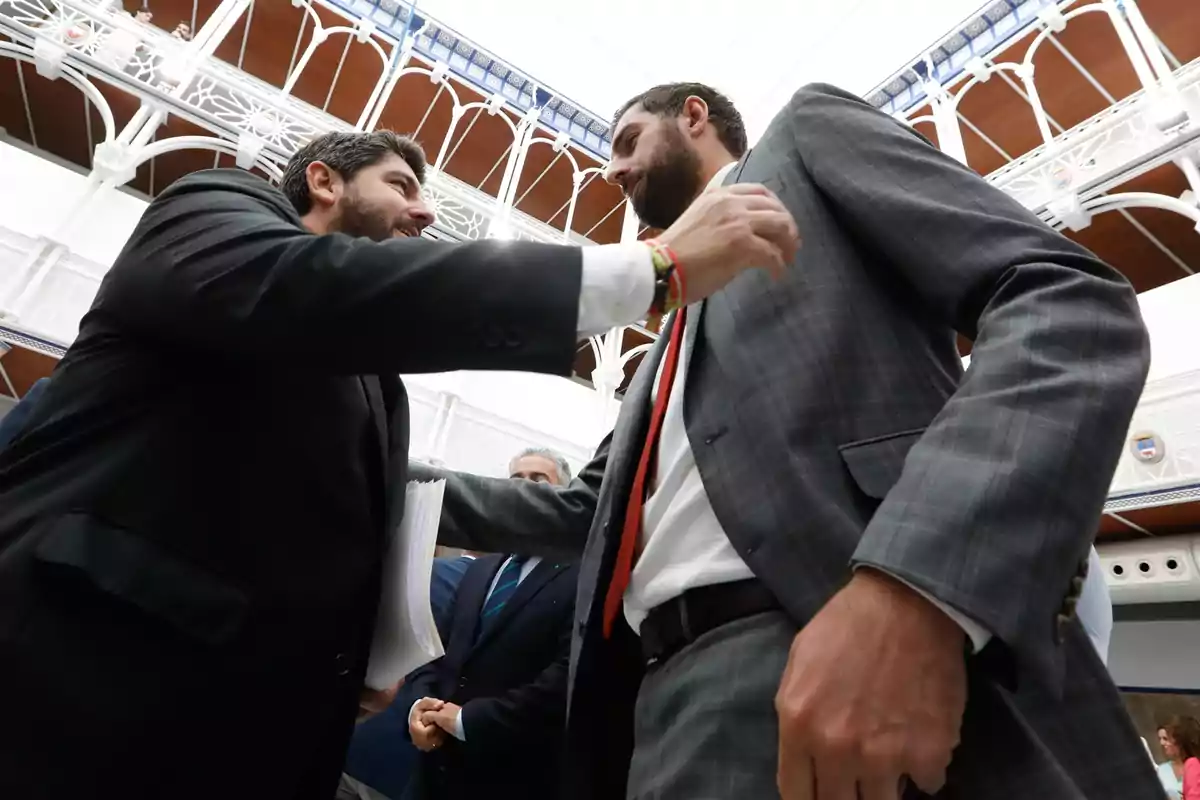 Dos hombres vestidos con traje se saludan de cerca en un edificio con arquitectura moderna y detalles blancos Dos hombres vestidos con traje se saludan de cerca en un edificio con arquitectura moderna y detalles blancos