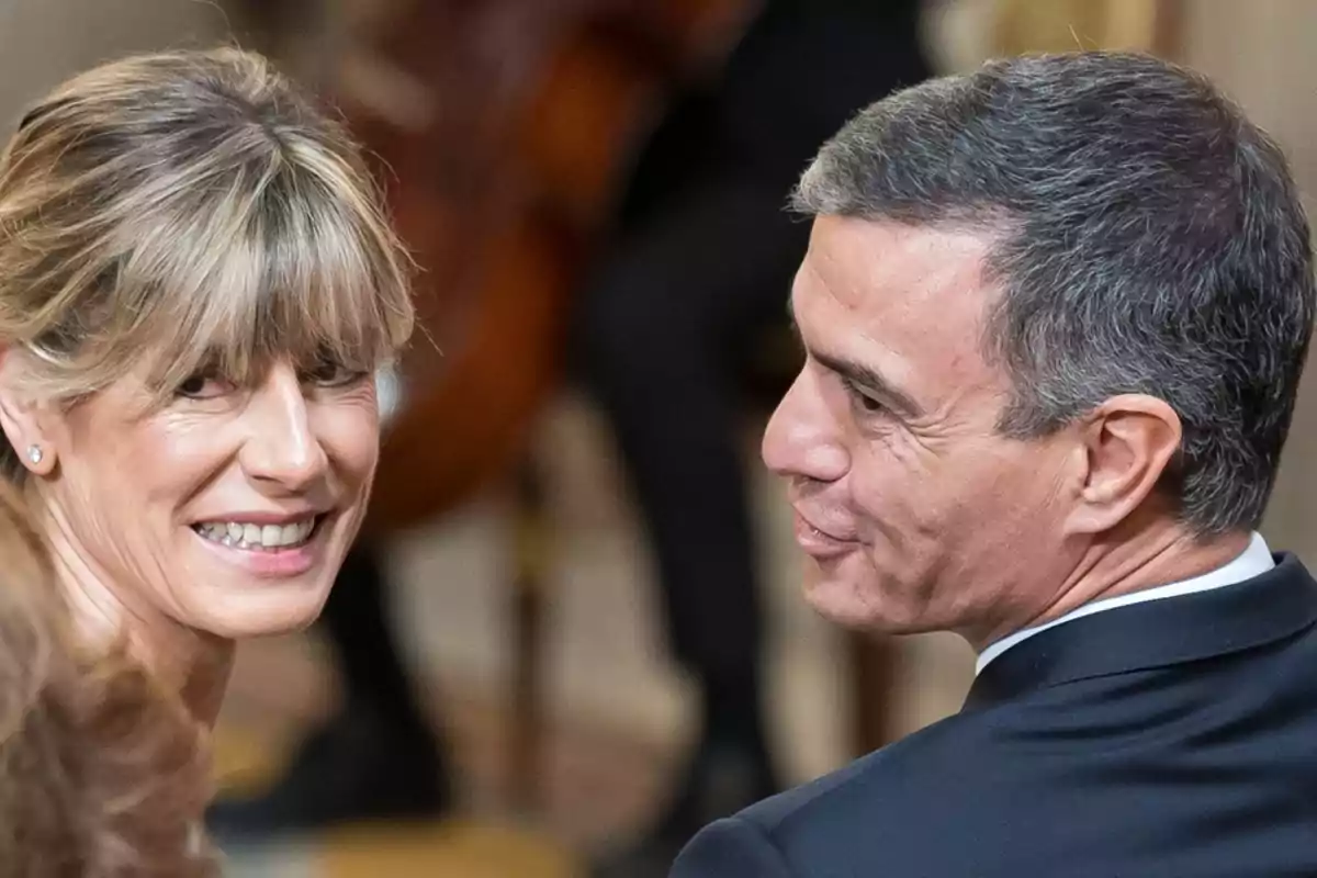 Dos personas sonrientes miran hacia atrás en un evento formal.