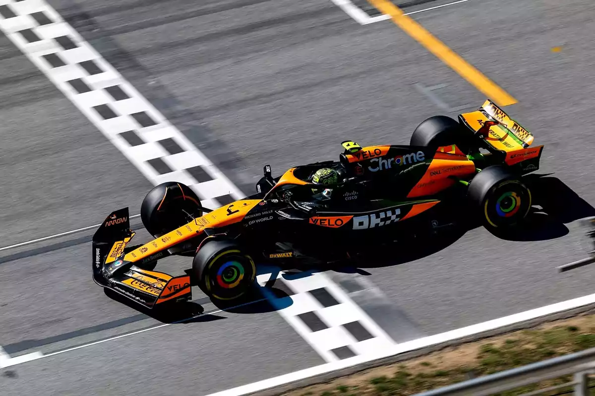 Un coche de Fórmula 1 de color naranja y negro cruza la línea de meta en un circuito de carreras.
