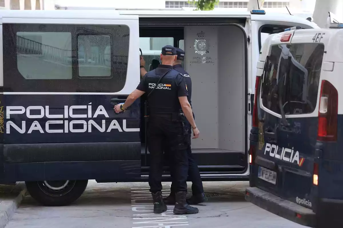 Dos agentes de la Policía Nacional junto a una furgoneta policial con la puerta trasera abierta.