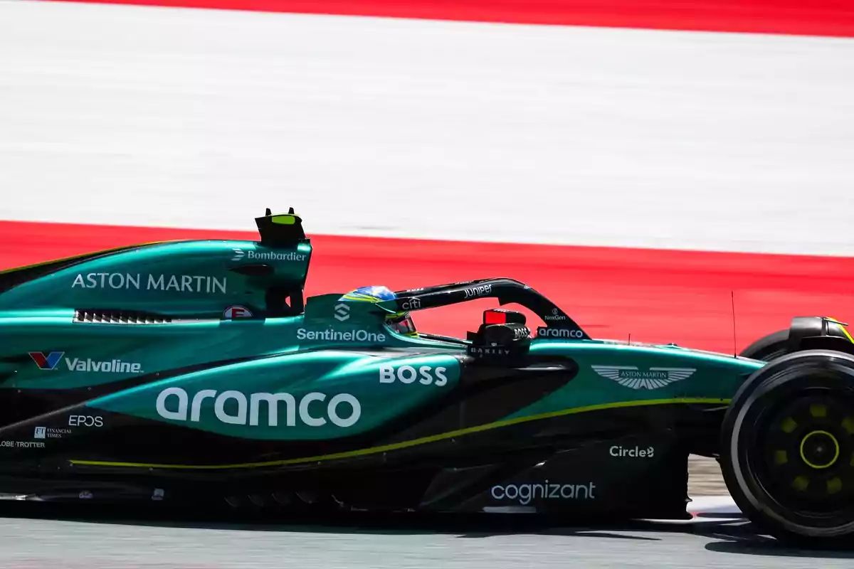 Un coche de carreras verde de la escudería Aston Martin compitiendo en una pista con fondo rojo y blanco.