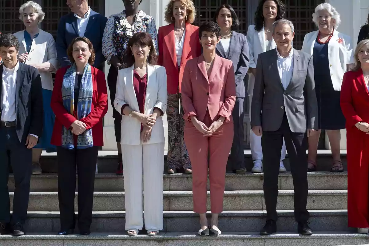 Un grupo de personas posando en una escalera, algunas de ellas vestidas con trajes formales y otras con ropa casual, en un entorno al aire libre frente a un edificio.