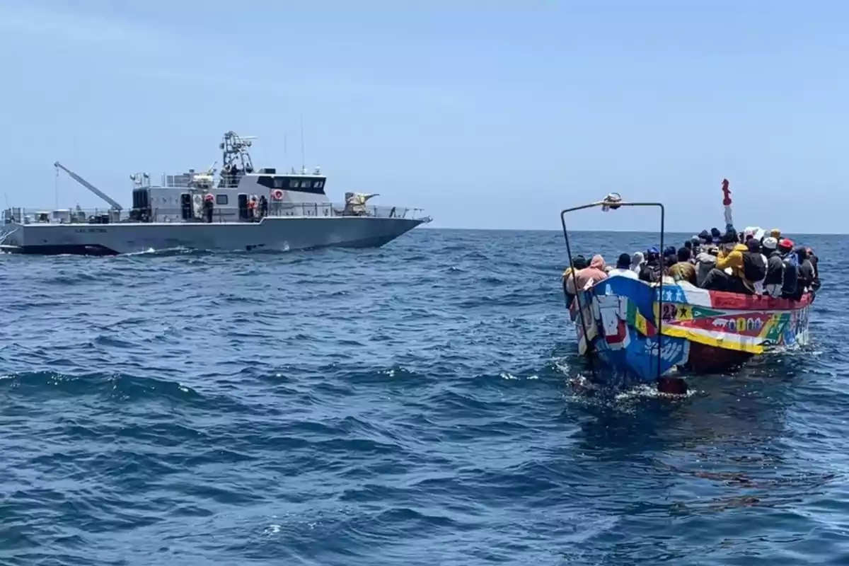 Un barco de la marina se acerca a una embarcación colorida llena de personas en el mar.