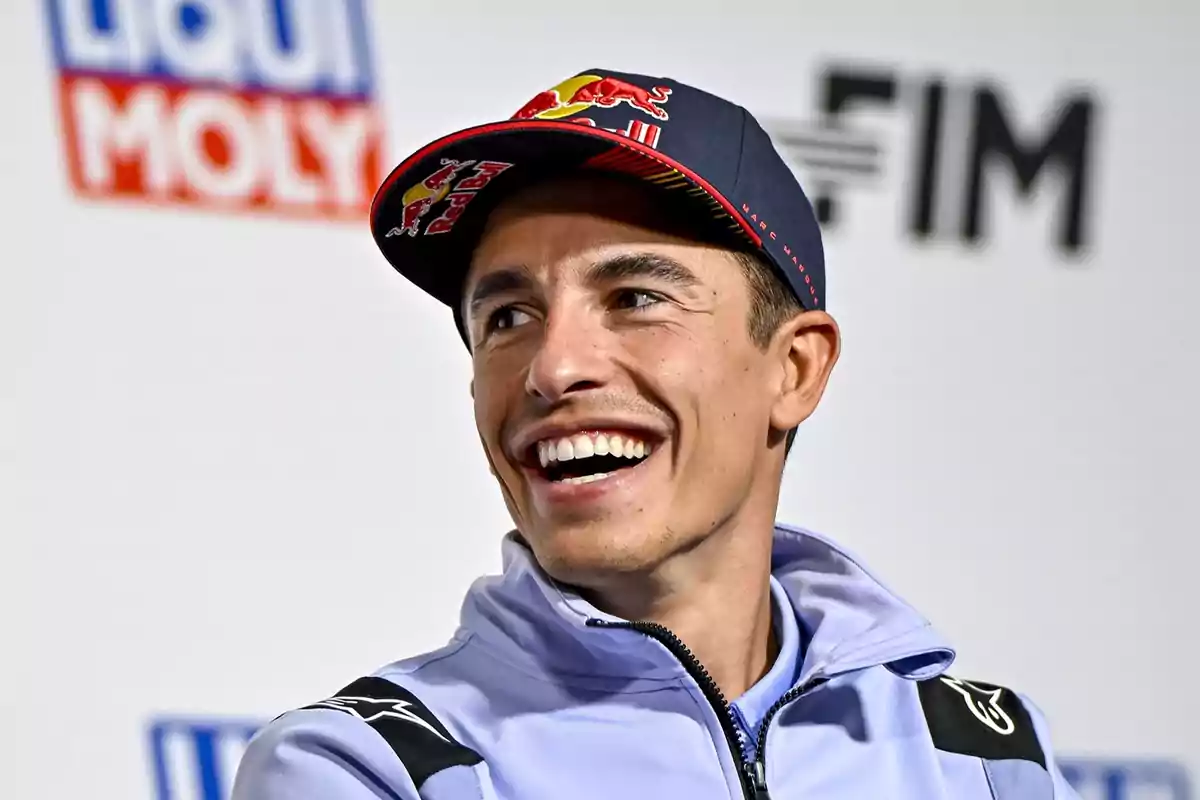 Un hombre sonriente con una gorra de Red Bull y una chaqueta deportiva en una conferencia de prensa.