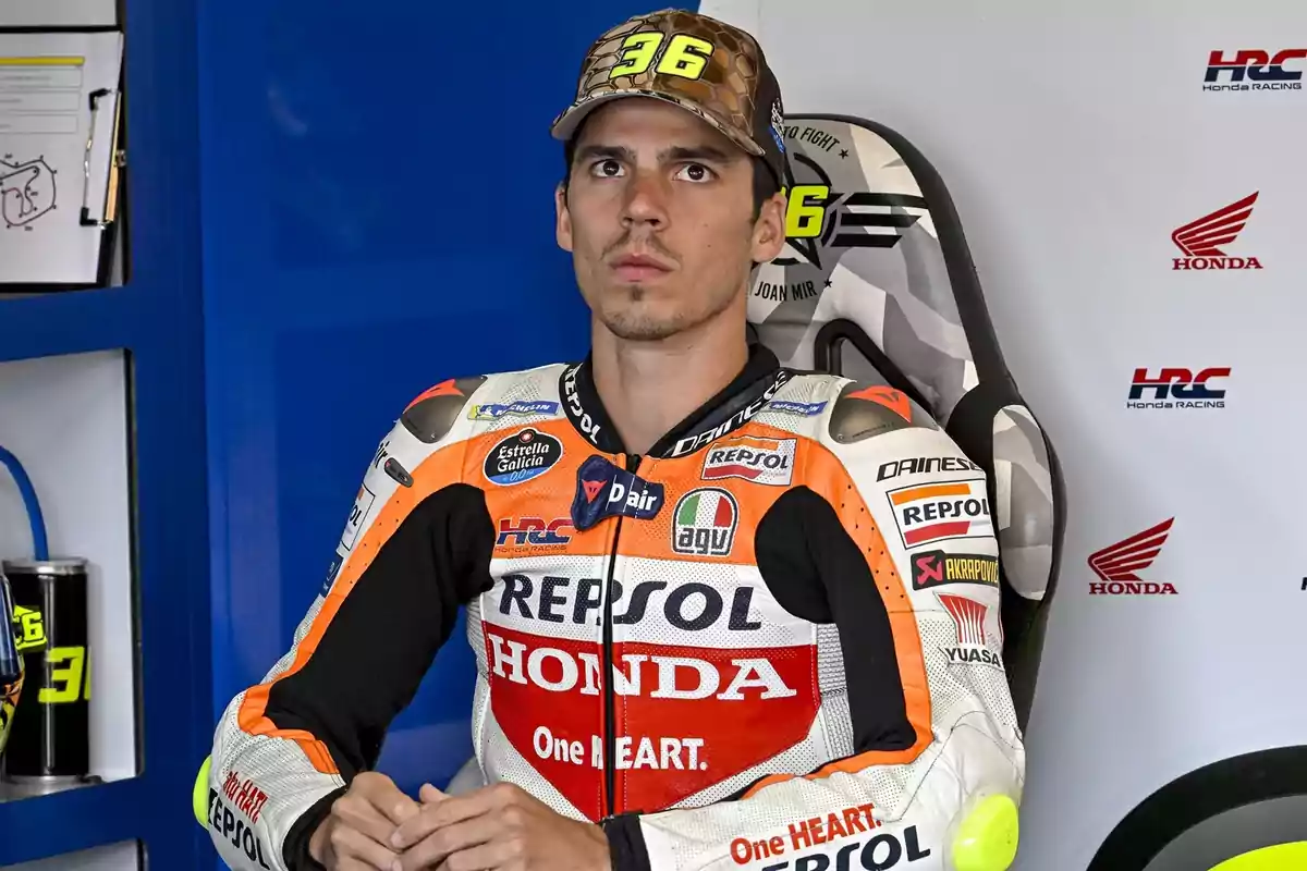 Un piloto de motociclismo con uniforme de Repsol Honda está sentado en una silla dentro de un garaje de equipo de carreras.