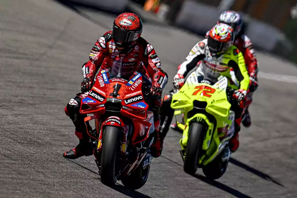 Tres motociclistas compitiendo en una carrera, con el piloto de la moto roja al frente seguido por otros dos pilotos en motos de colores brillantes.