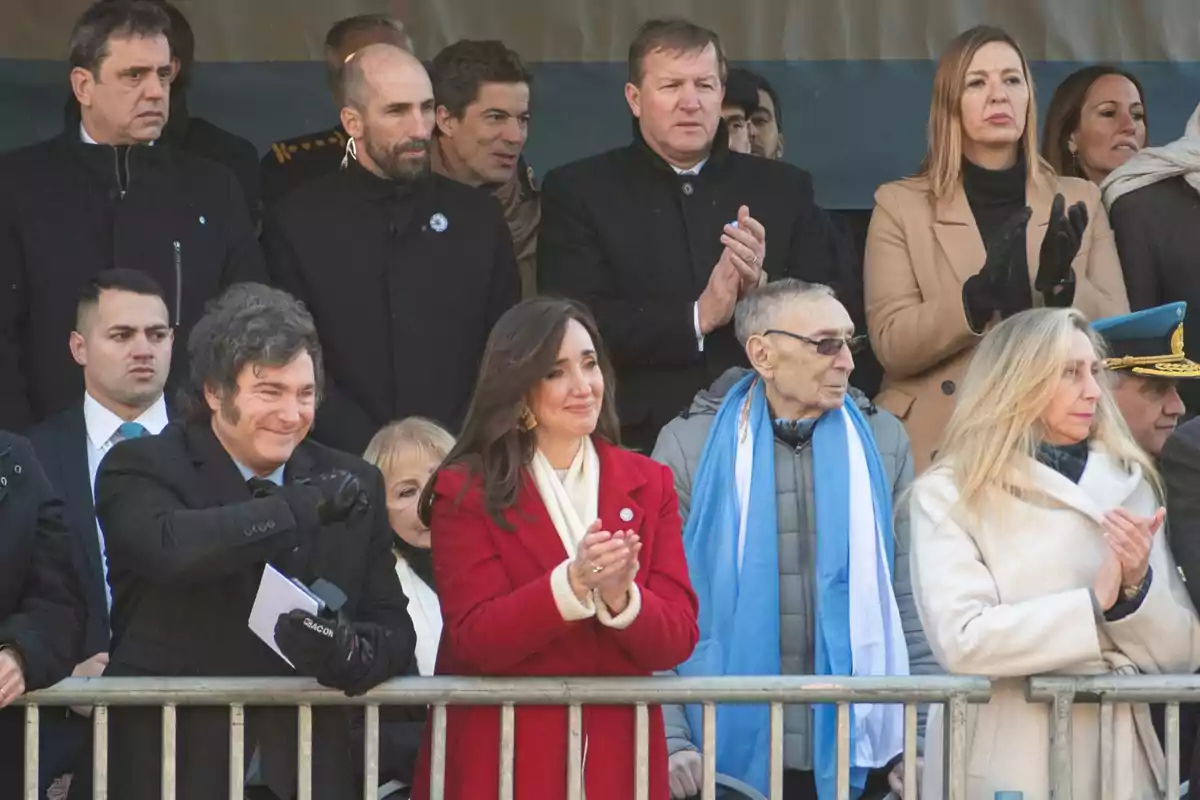 Un grupo de personas aplaudiendo en un evento al aire libre, algunas de ellas vestidas con abrigos y bufandas debido al clima frío.