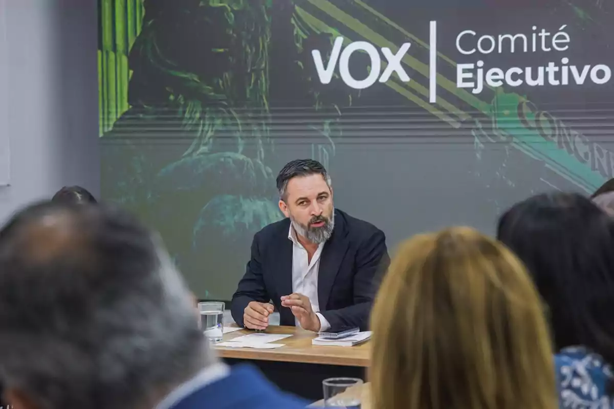 Un hombre hablando en una reunión del Comité Ejecutivo de VOX con un fondo que muestra el logo del partido.