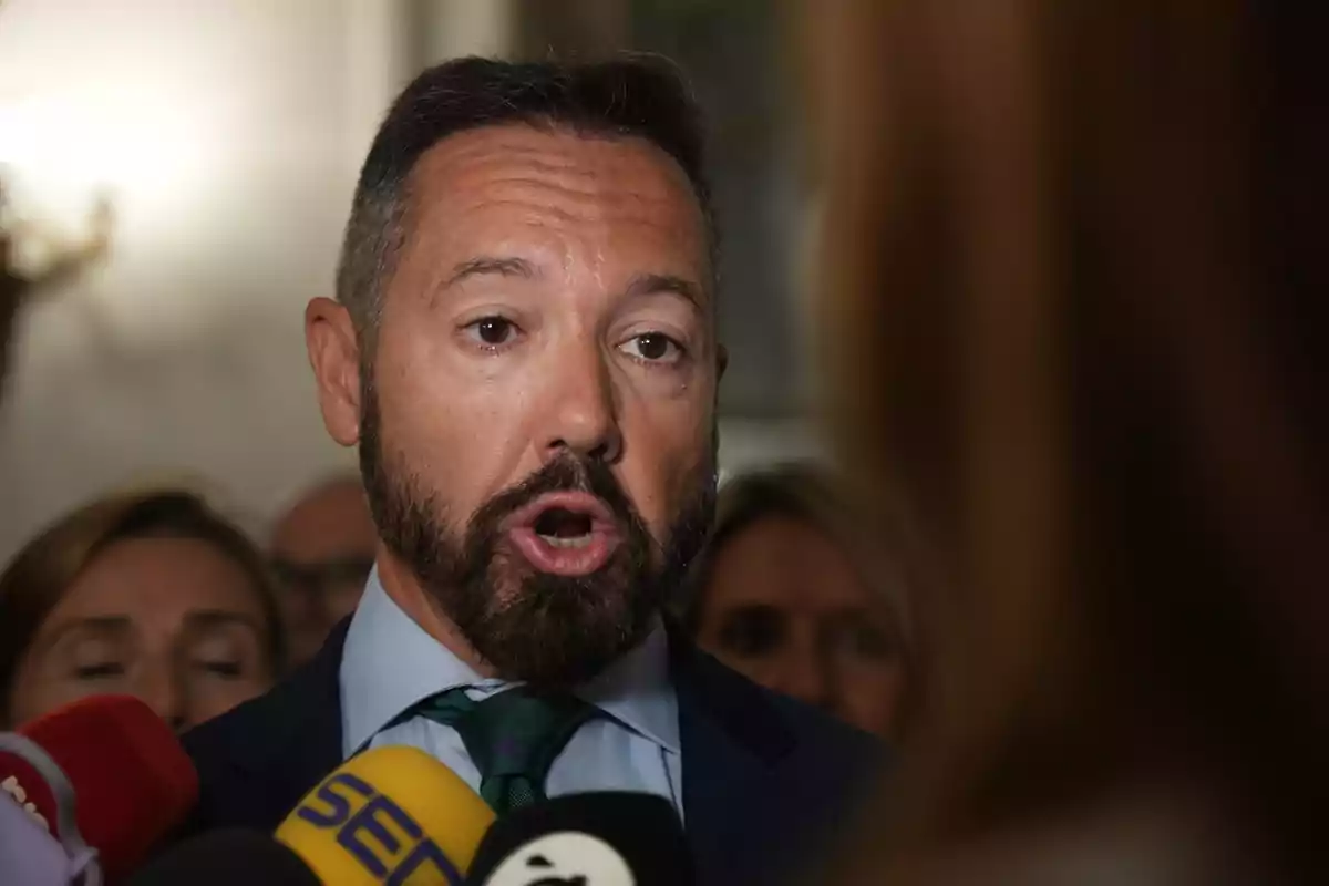 A man speaking in front of several press microphones.