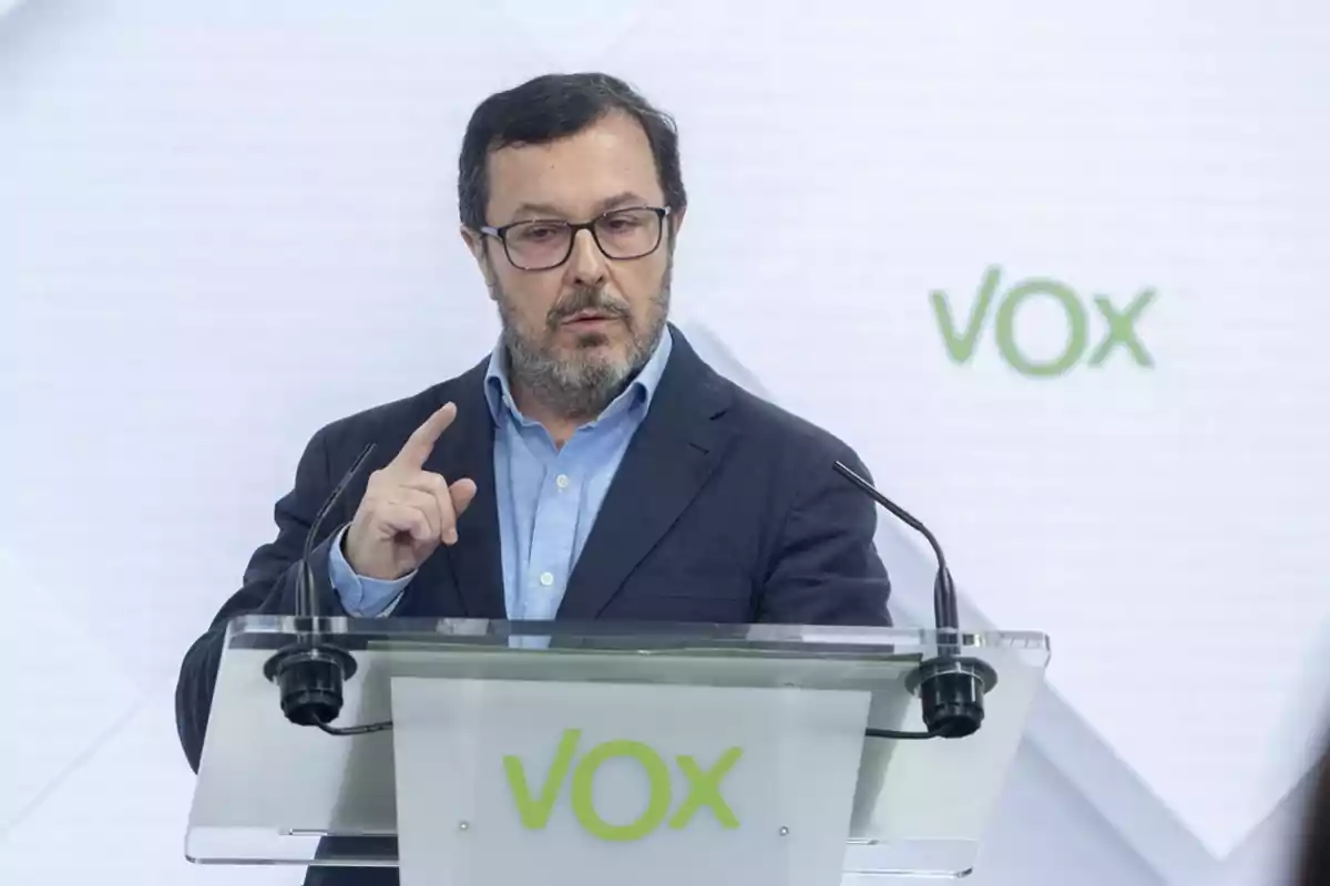 Un hombre con barba y gafas habla en un podio con el logotipo de Vox.