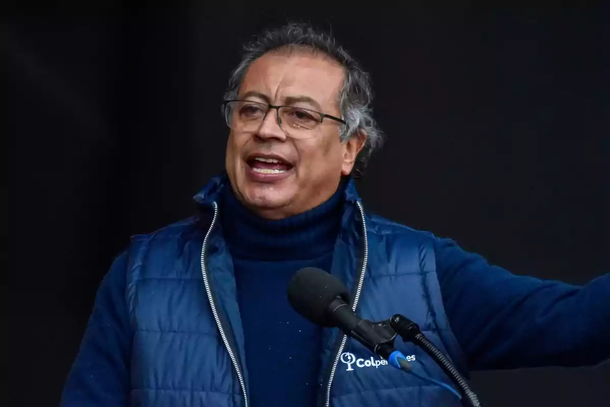 Hombre con gafas y chaqueta azul hablando en un micrófono.