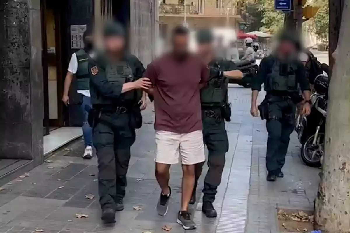 A group of police officers escorts a handcuffed man down an urban street.