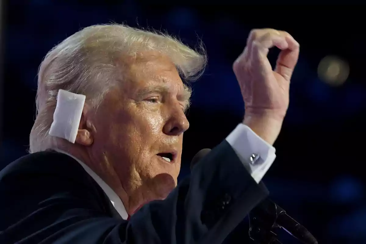 Hombre de cabello canoso con un vendaje en la oreja, hablando y gesticulando con la mano.