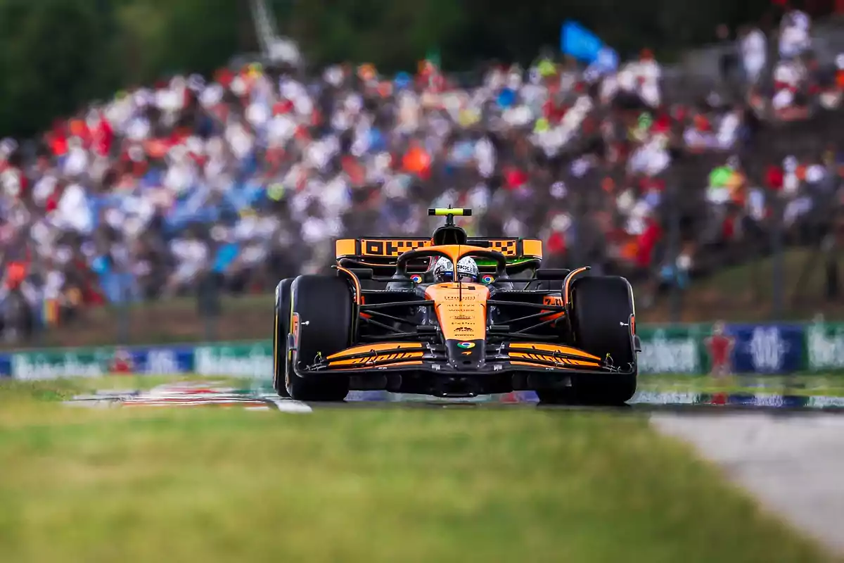 Un coche de Fórmula 1 naranja y negro en la pista con una multitud de espectadores al fondo.