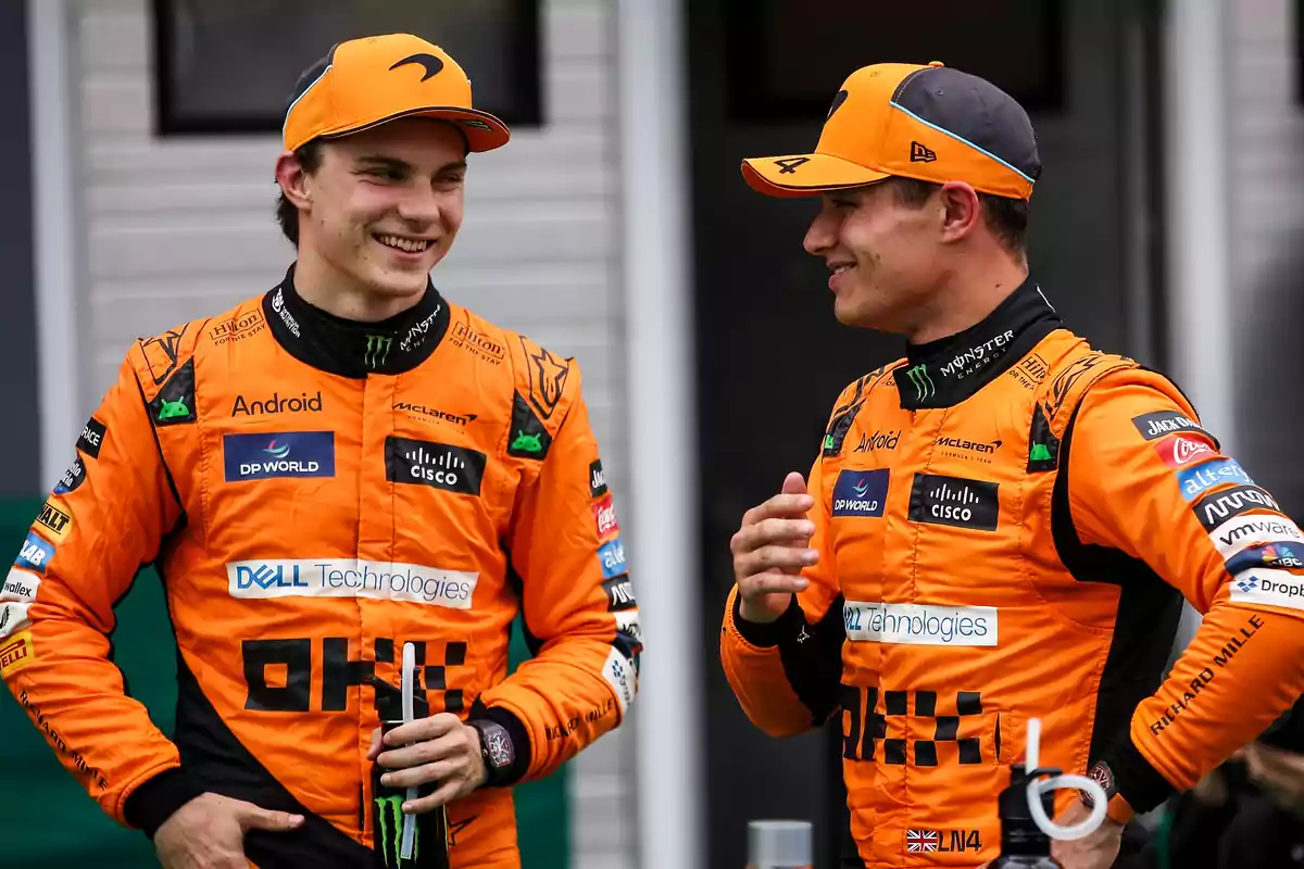 Dos pilotos de carreras con trajes naranjas de McLaren conversan y sonríen.