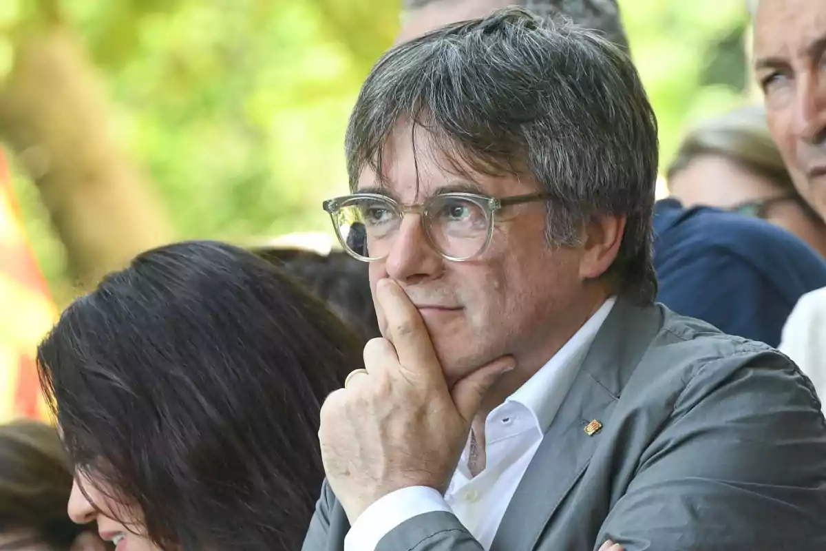 Un hombre con gafas y chaqueta gris pensativo en un entorno al aire libre.