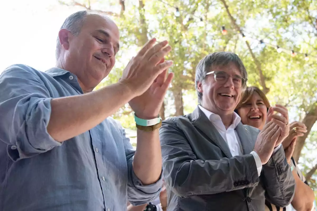 Personas aplaudiendo al aire libre en un evento con árboles de fondo.