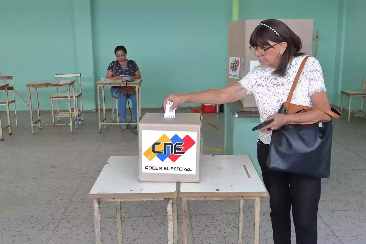 Una mujer deposita su voto en una urna electoral mientras otra persona supervisa en un centro de votación.