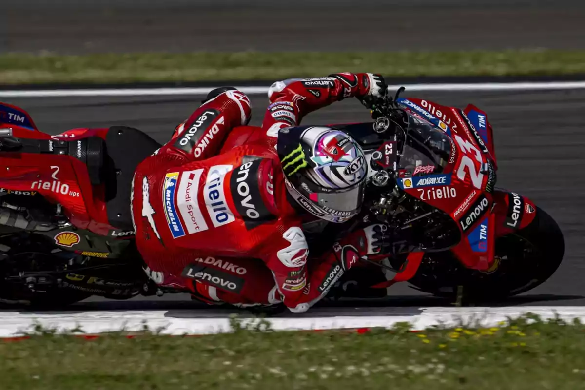 Motociclista en una curva durante una carrera de motociclismo, vistiendo un traje rojo y montando una motocicleta roja con varios logotipos de patrocinadores.