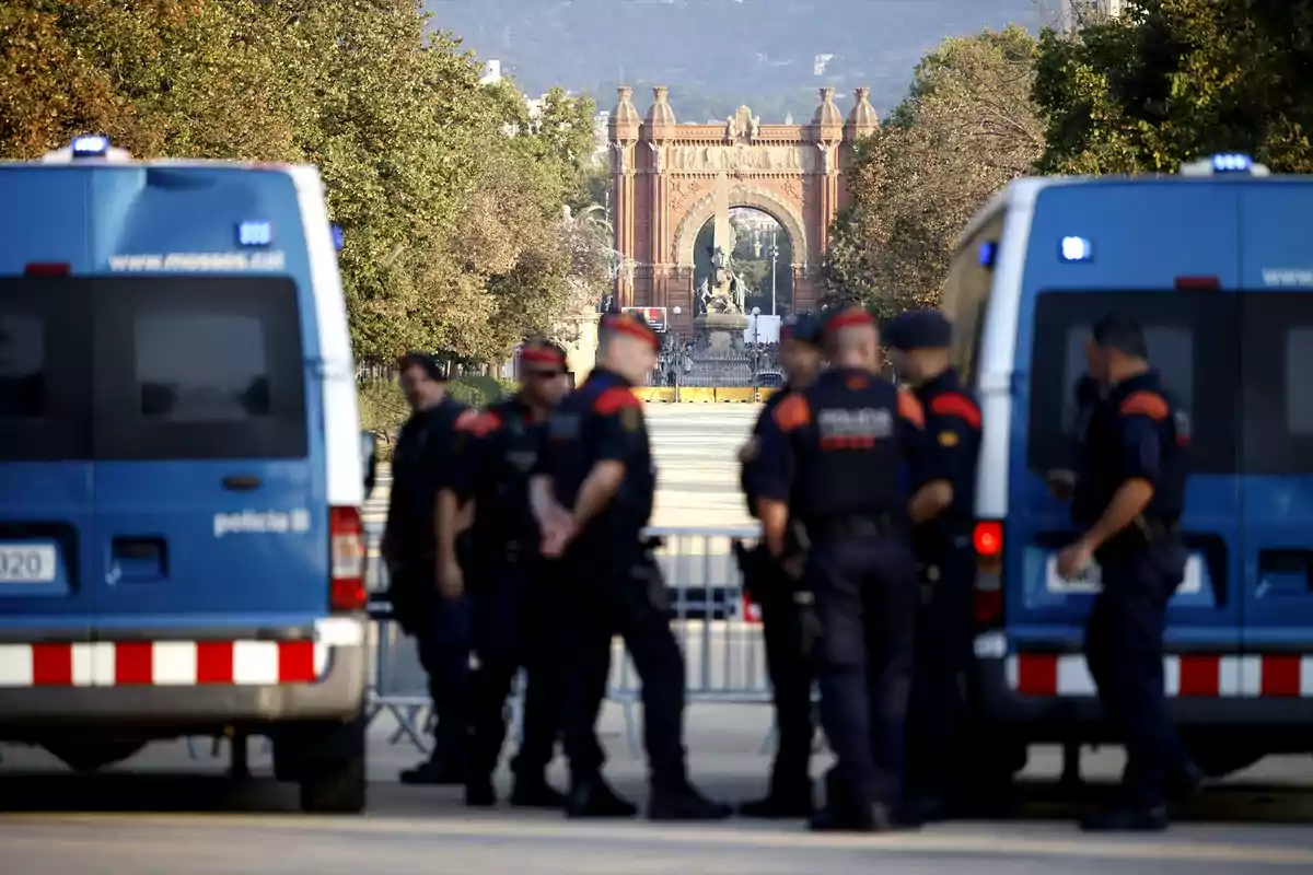 Un grupo de policías se encuentra frente a dos furgonetas azules con el Arco de Triunfo al fondo.