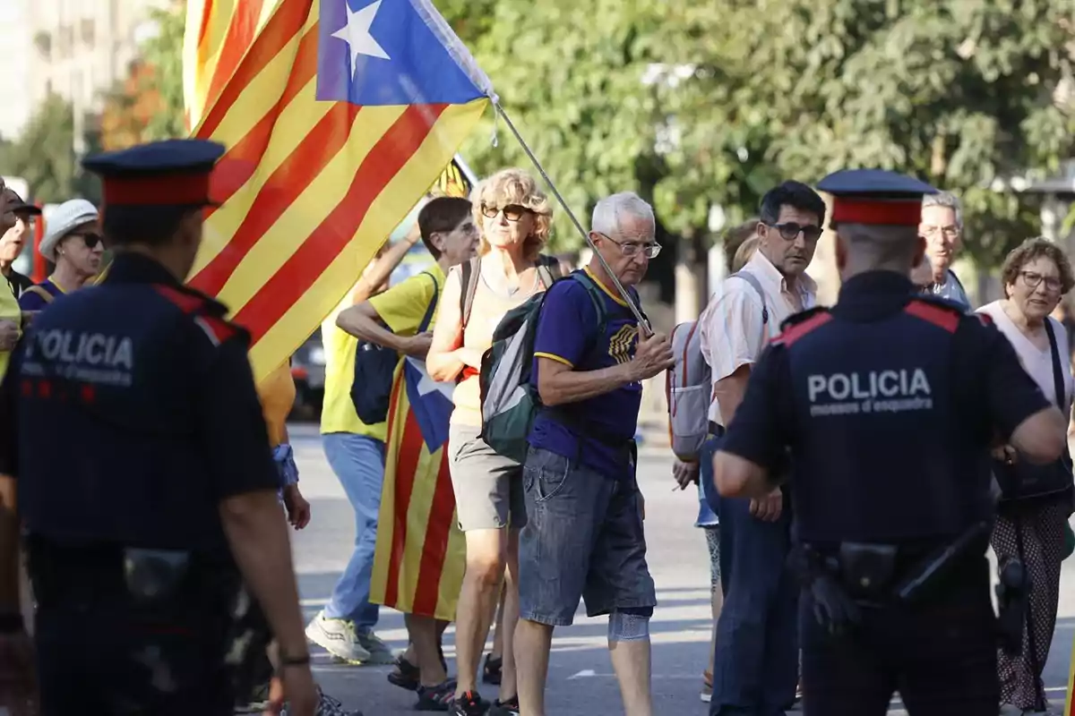 Un grupo de personas con banderas catalanas es observado por dos policías en una calle.