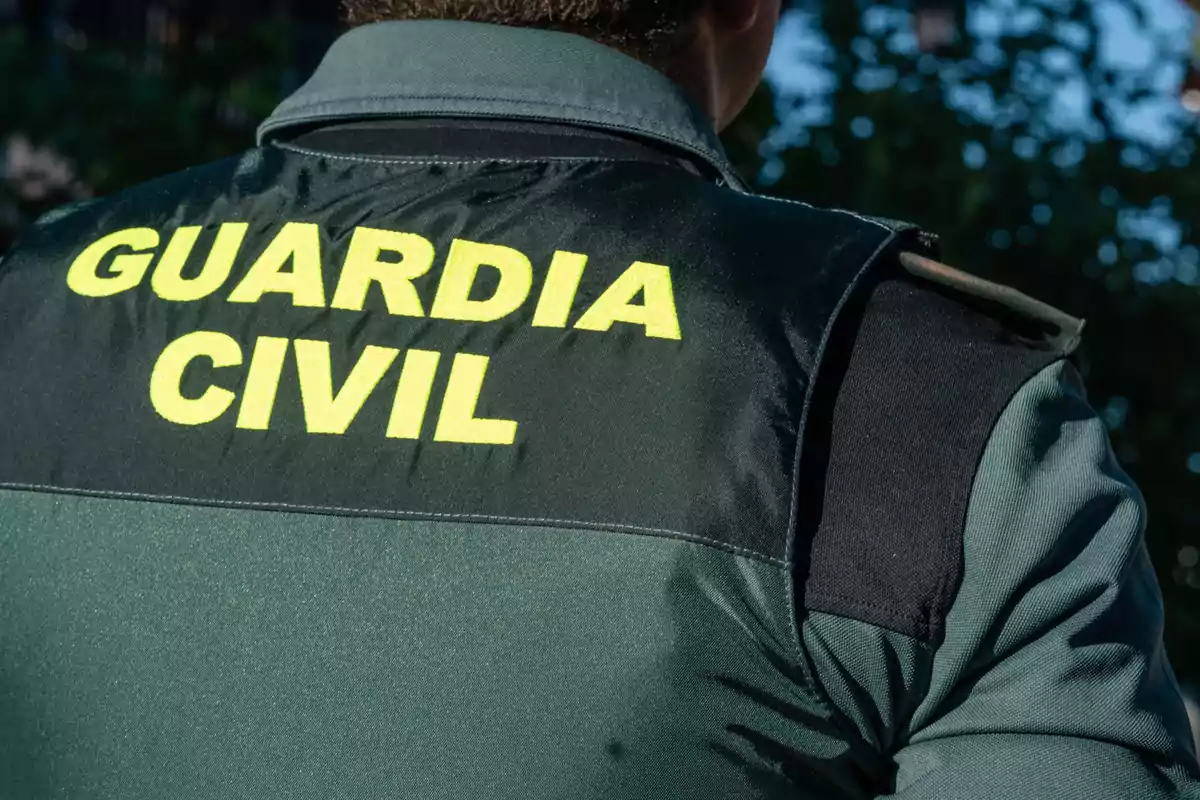 Un agente de la Guardia Civil visto desde atrás con el uniforme verde y letras amarillas.