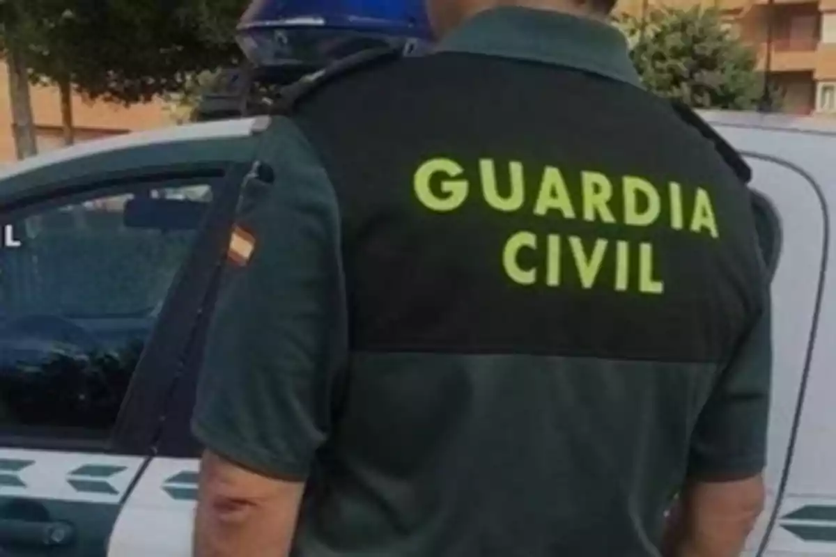 Un agente de la Guardia Civil de espaldas junto a un coche patrulla.