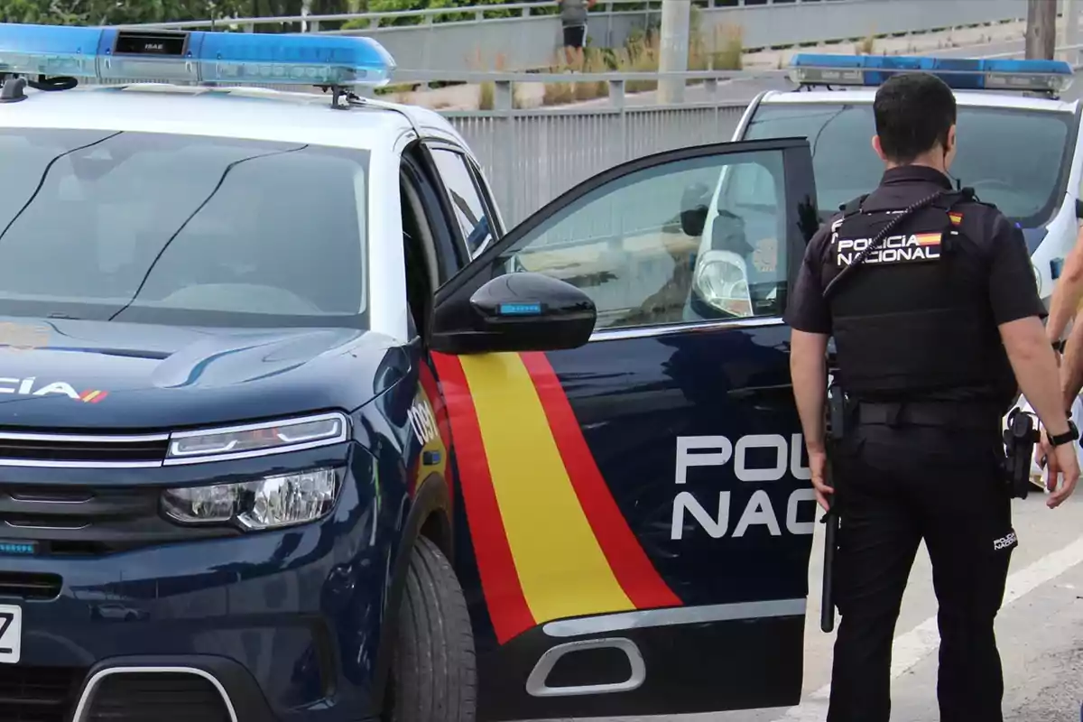 Un agente de la Policía Nacional junto a un coche patrulla con las puertas abiertas.