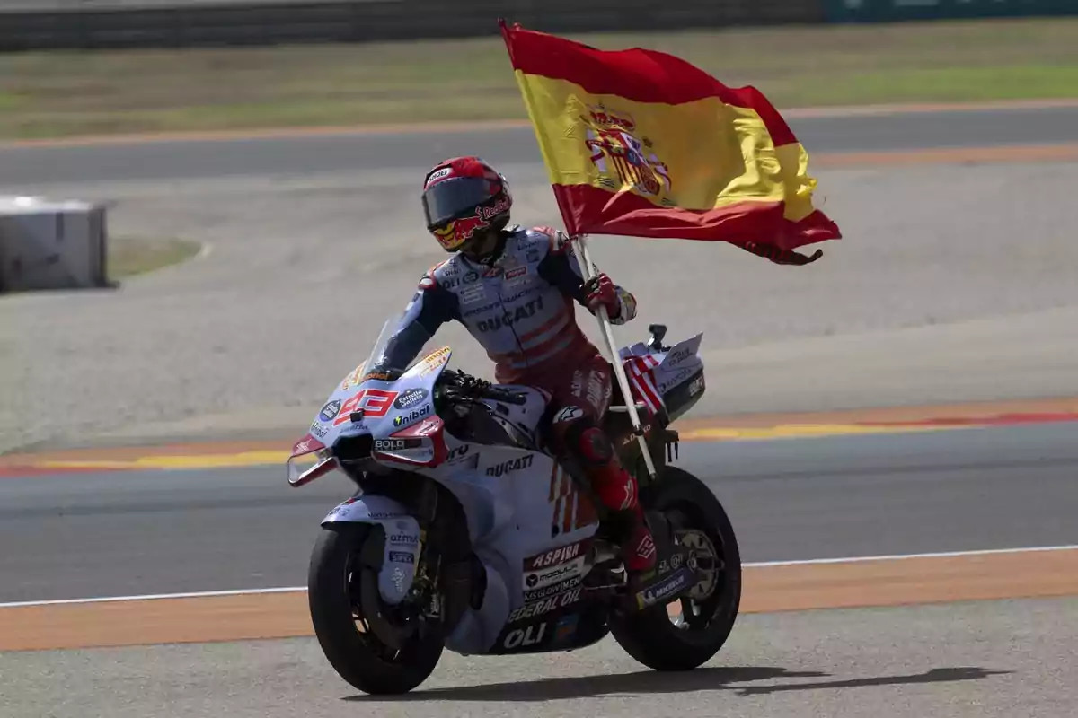 Un motociclista celebrando con una bandera de España en un circuito de carreras.