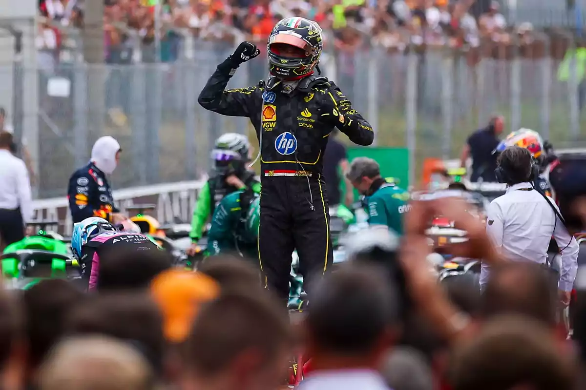 Un piloto de carreras celebra con el puño en alto mientras la multitud lo observa en el fondo.