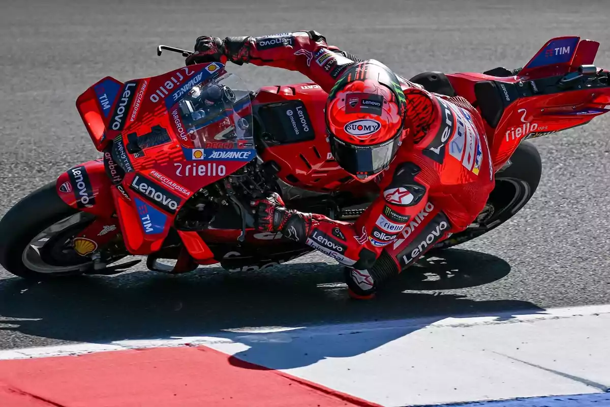 Motociclista en una curva durante una carrera de motociclismo, con traje y motocicleta rojos llenos de patrocinadores.