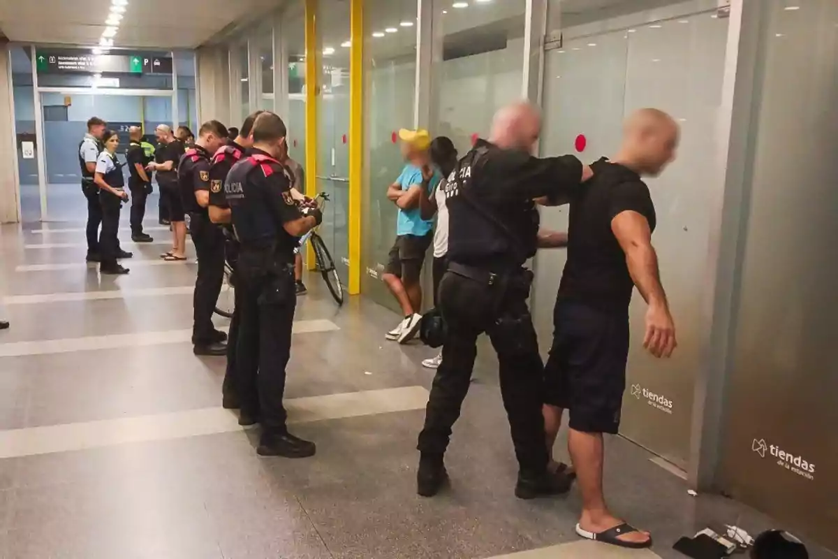 Policías revisando a varias personas en un pasillo de un edificio.