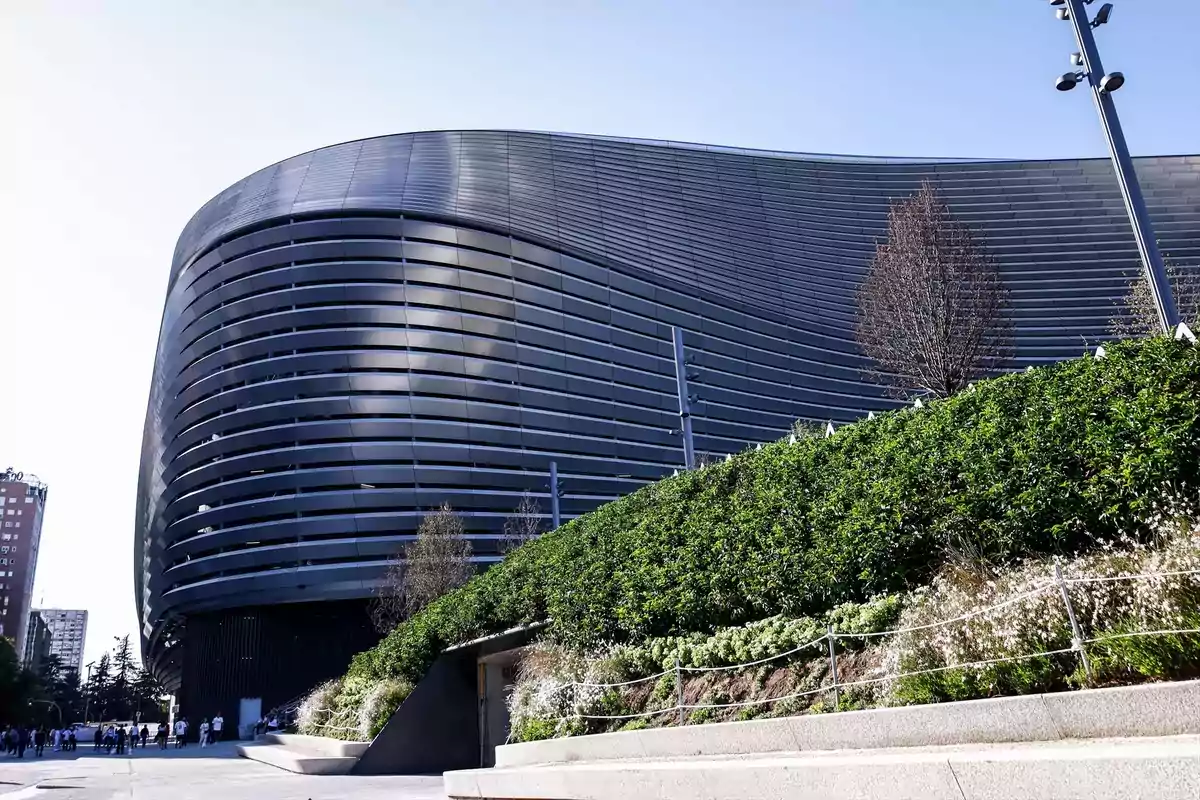 Edificio moderno con fachada curva y jardín en primer plano.