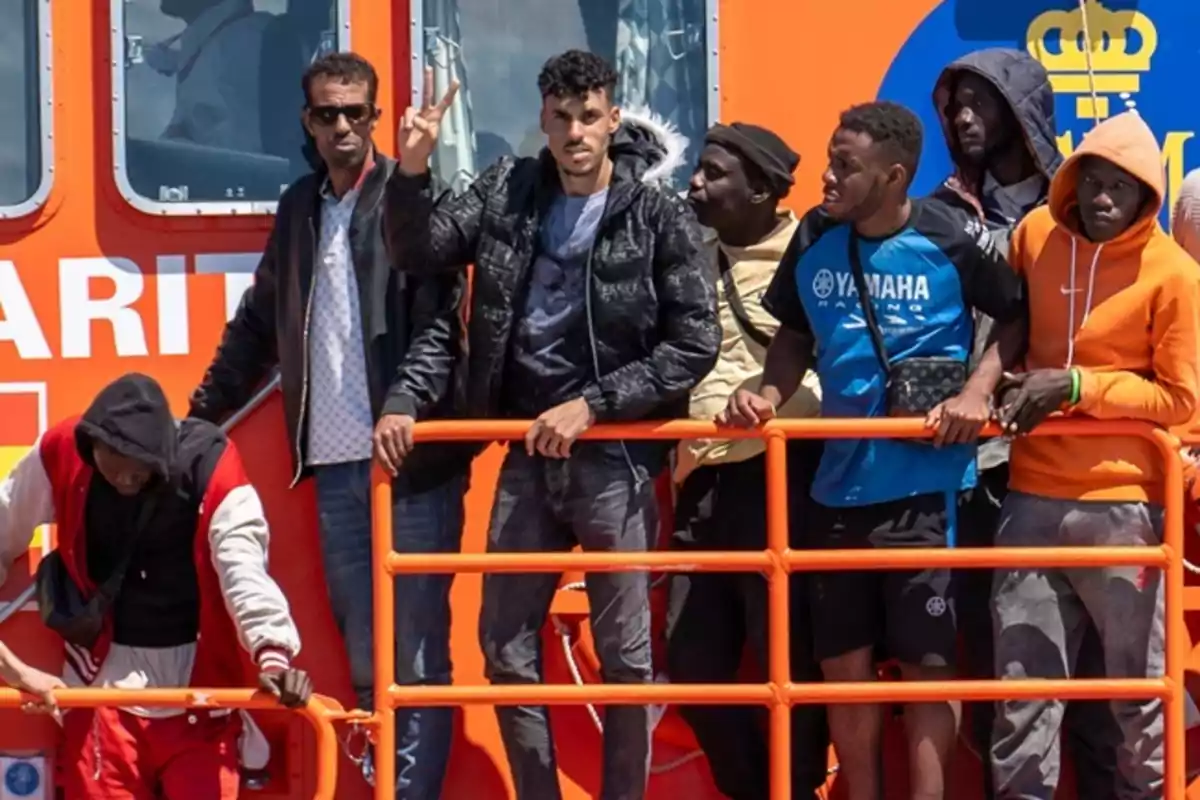 Un grupo de personas de pie en la cubierta de un barco de rescate con barandillas naranjas.