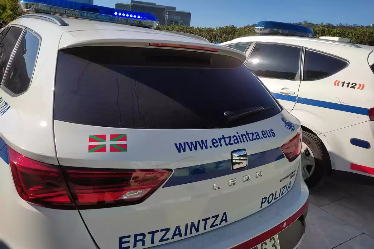 Dos coches de policía de la Ertzaintza estacionados uno al lado del otro con luces azules en el techo y la bandera del País Vasco en la parte trasera.