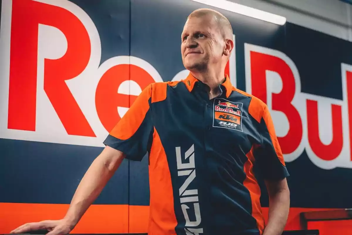 Hombre con camisa de equipo de carreras Red Bull KTM posando frente a un cartel de Red Bull.