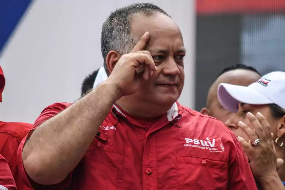 Un hombre con camisa roja hace un gesto con la mano en un evento público.