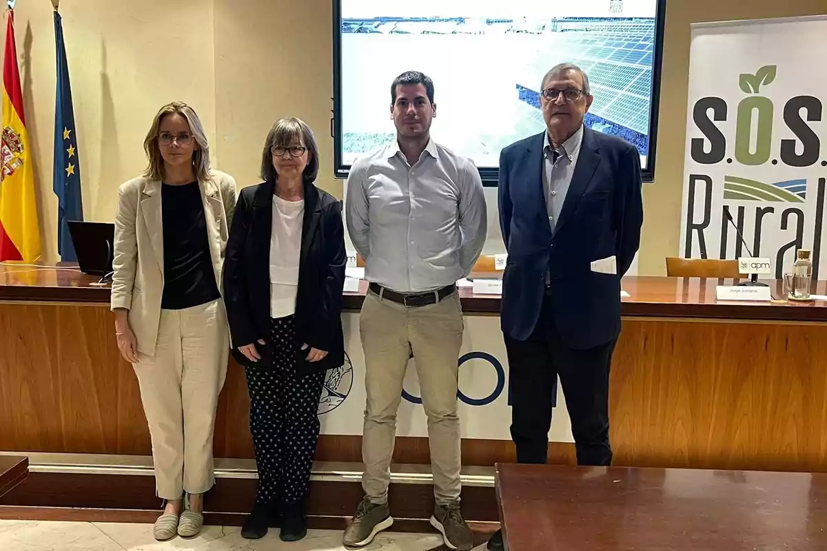 Cuatro personas posan frente a una mesa de conferencias con banderas de España y la Unión Europea al fondo y un cartel que dice "s.o.s. Rural".