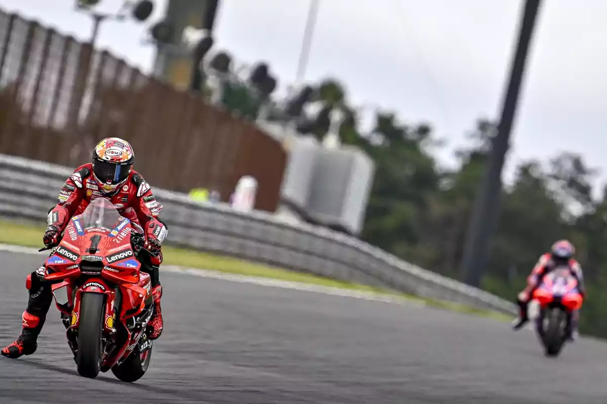 Dos motociclistas compiten en una pista de carreras, uno en primer plano y otro más atrás, ambos con trajes y motos rojas.