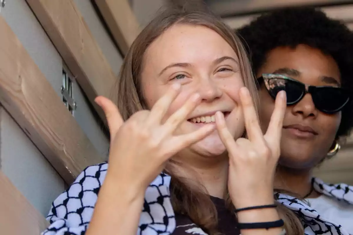 Two smiling people, one of them making a gesture with their hands, while together in a casual setting.