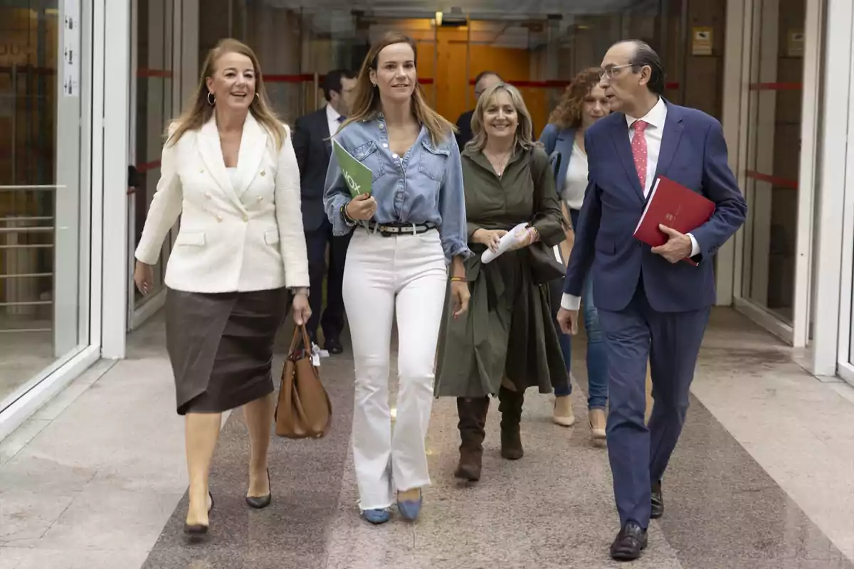 Un grupo de personas caminando juntas por un pasillo, algunas llevan carpetas y otras bolsos.