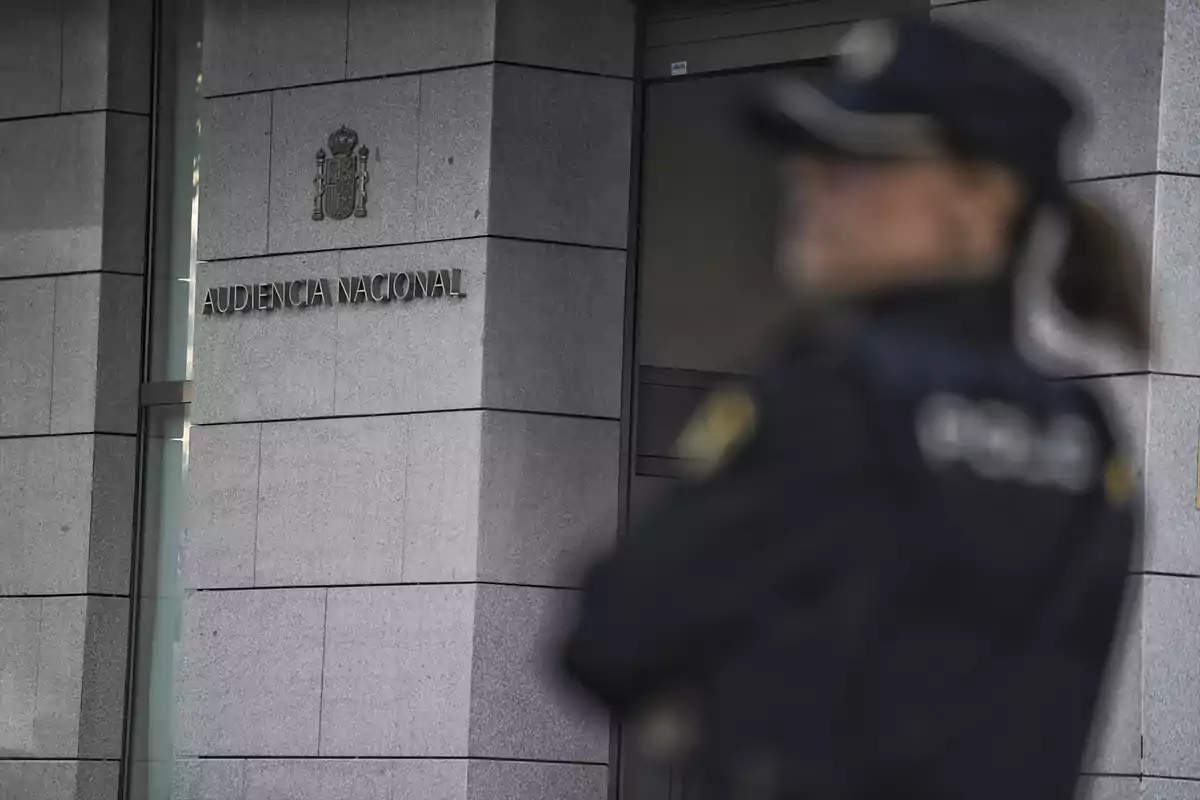 Fachada de la Audiencia Nacional con una figura policial desenfocada en primer plano.