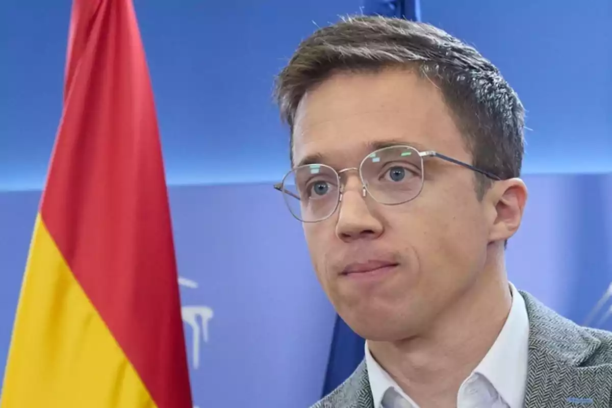 Un hombre con gafas y una bandera de fondo.