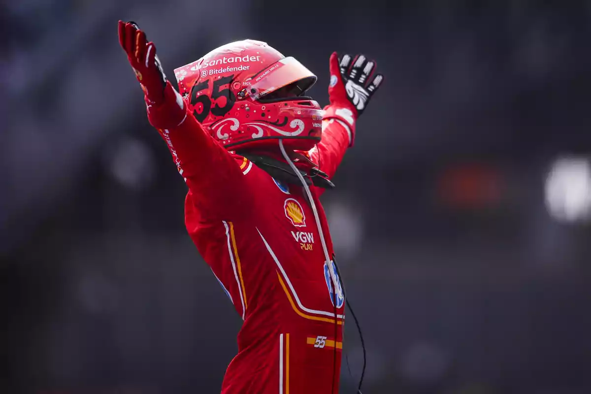 Piloto de carreras con traje rojo y casco levantando los brazos en señal de victoria.