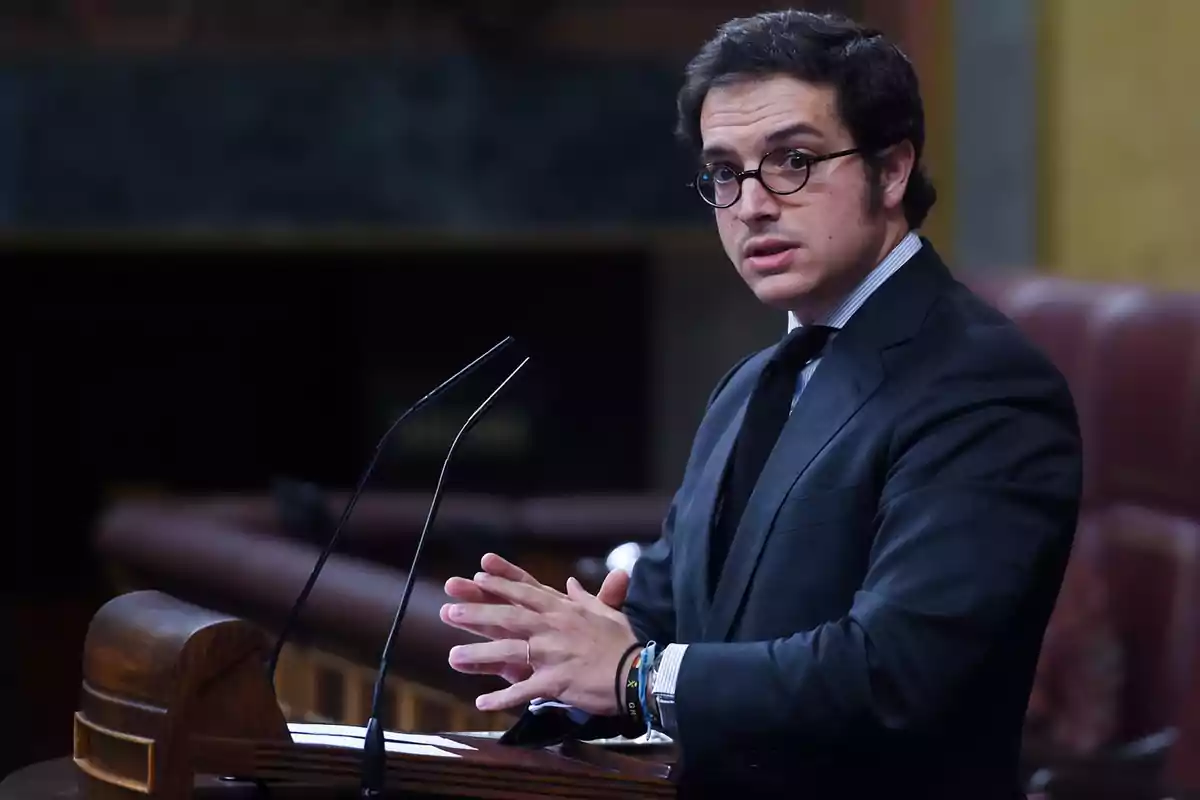 Hombre con gafas y traje oscuro hablando en un podio.