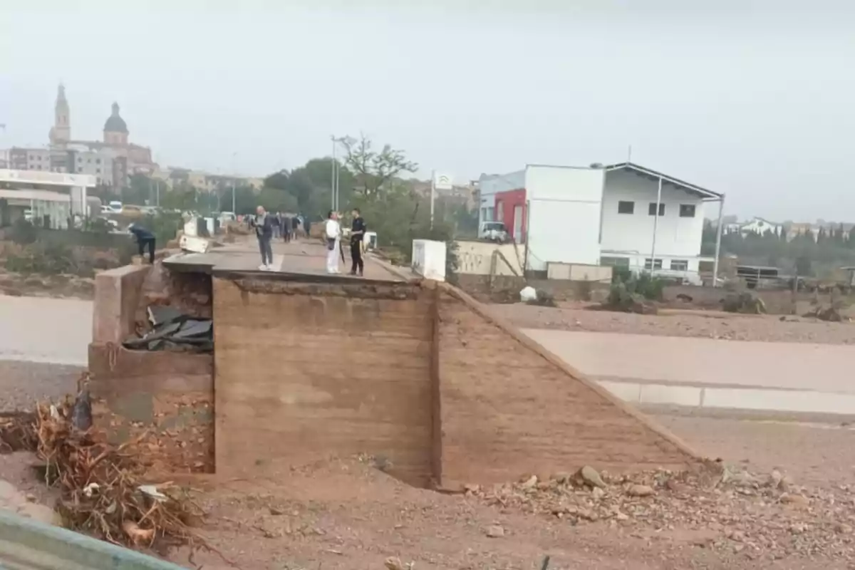 Personas observando un puente colapsado en un área urbana después de una inundación.